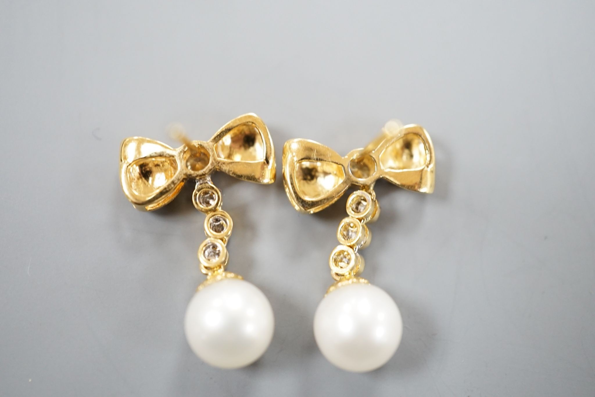 A modern pair of 750 yellow metal, cultured pearl and diamond set ribbon bow drop earrings